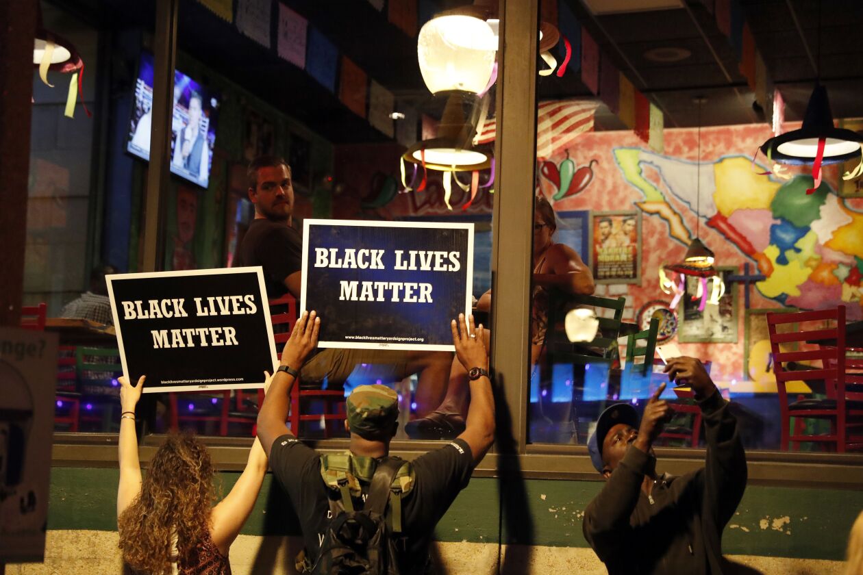 Protesters hold up signs as restaurant patrons look out the window in St. Louis, after a judge found a white former St. Louis police officer, Jason Stockley, not guilty of first-degree murder in the death of a black man, Anthony Lamar Smith, who was fatal